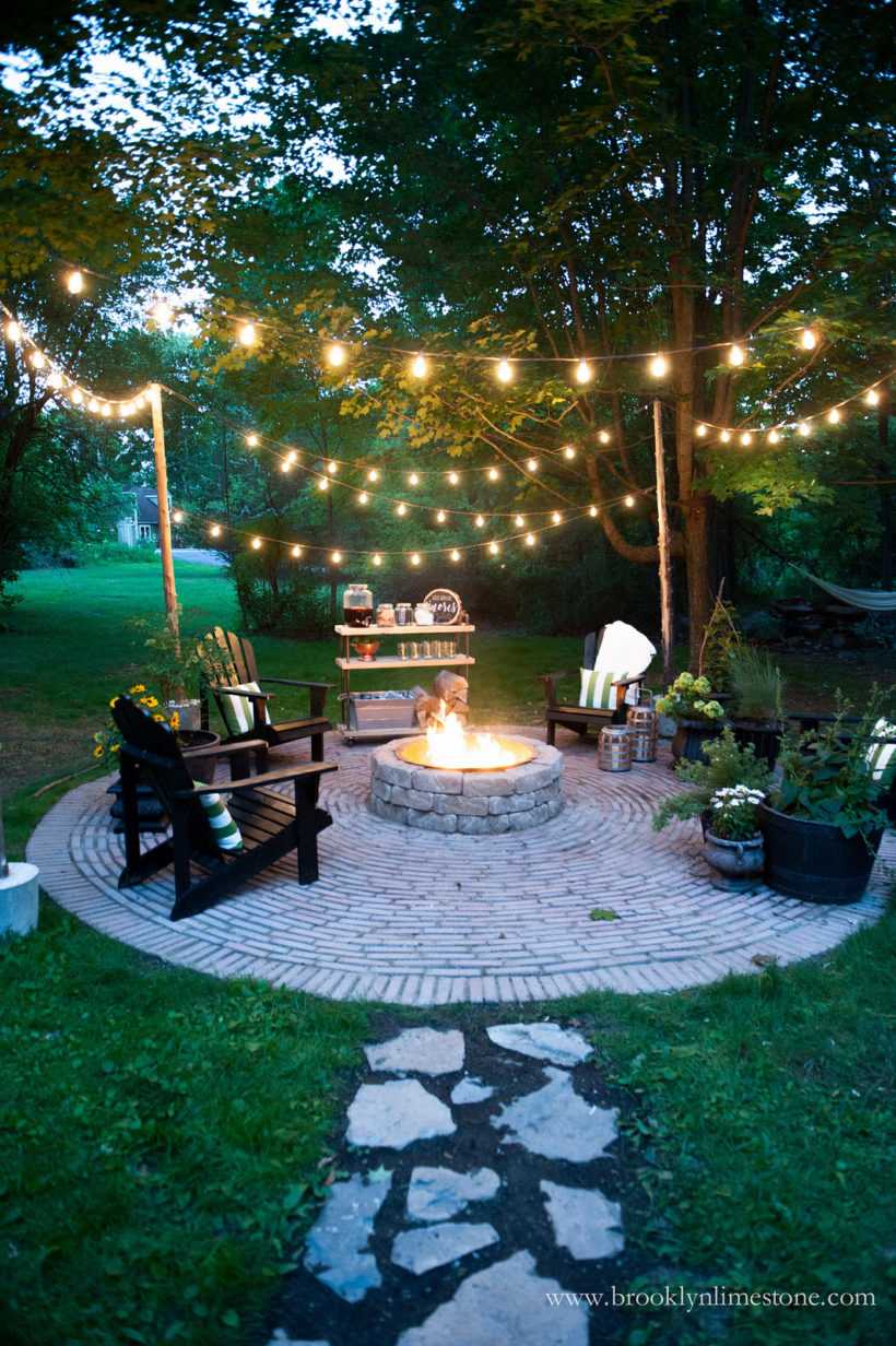 A beautiful circular paved area provides the perfect space for a DIY fire pit to stay center stage. Add some string lighting for even more ambience! Via Brooklyn Limestone